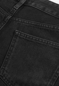 Zwarte denim stof met een gladde textuur, voorzien van een enkele achterzak en contrasterende stiknaad langs de randen.
