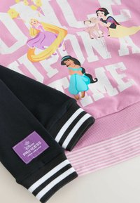 Sweatshirt rose avec des princesses Disney, manches noires à rayures blanches, et une étiquette violette portant les mots "Disney PRINCESS."