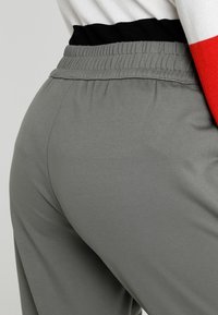 Grijze joggerbroeken met een zachte textuur, voorzien van een elastische tailleband en een contrasterende zwart-rode streep bovenaan.