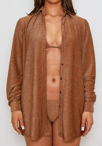 Camisa de botones marrón brillante en un tejido suave, abierta en la parte delantera, superpuesta a un conjunto de bikini a juego, que presenta un diseño minimalista.