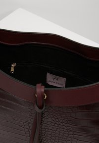 Burgundinpunainen krokotiilikuviollinen nahkainen olkalaukku, jossa sileä pinta, vetoketjutasku ja sisällä logotunniste.