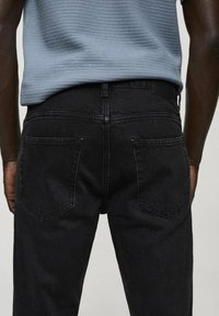 Jeanși negri din denim cu croială slim, având buzunare la spate și un design drept al picioarelor. Țesătura are o textură netedă și o ușoară strălucire.