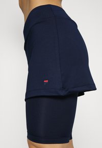 Falda deportiva azul marino sobre pantalones cortos ajustados a juego, hecha de un tejido elástico. Incluye un pequeño logo con acentos rojos y negros en el dobladillo.