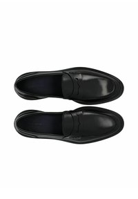 Mocasines de cuero negro con un acabado suave, que presentan costuras decorativas y un sutil diseño elevado en la parte delantera. Suela plana, estilo de poner y quitar.