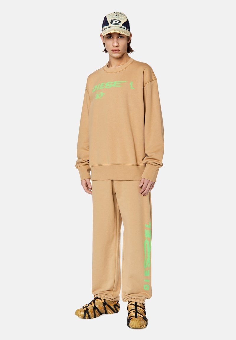 Felpa oversize beige con logo "DIESEL" verde, pantaloni beige abbinati e sandali neri e gialli. Design casual e dal taglio rilassato.