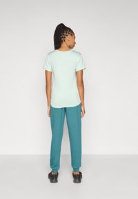 Τιρκουάζ φόρμα και ανοιχτό πράσινο t-shirt, και τα δύο κατασκευασμένα από μαλακό ύφασμα. Το t-shirt έχει κοντά μανίκια και στρογγυλή λαιμόκοψη.