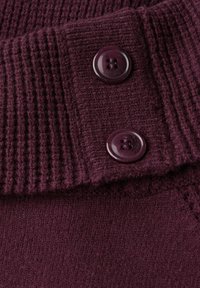 Bordeauxroter gerippter Strickstoff mit zwei dunkelbordeauxfarbenen Knöpfen im 4-Loch-Design. Glatte Textur unterhalb des Knopfbereichs.