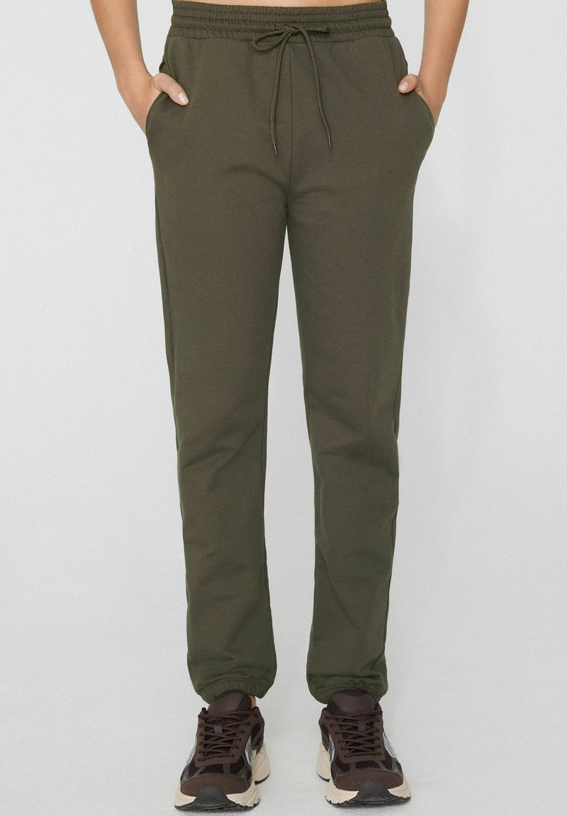 Olivově zelené tepláky s elastickým pasem a nastavitelným stahovacím páskem, vybavené bočními kapsami a zúženým střihem nohavic.