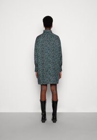 Robe à imprimé floral avec des manches longues, un col haut et une coupe décontractée. Fond sombre avec des motifs bleus et blancs. Bottes noires jusqu'aux genoux.