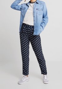 Jasnoniebieska koszula dżinsowa na szarym topie, w połączeniu z granatowymi spodniami w białe wzory oraz szarymi tenisówkami.