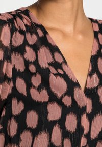 Černá tkanina s růžovými abstraktními skvrnami, s designem výstřihu do V a jemnou strukturou, s leskem odrážejícím se v materiálu.