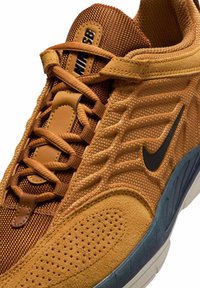 Brązowy sneaker Nike SB z siateczkowymi i zamszowymi materiałami, czarnym logo swoosh, starannym przeszyciem oraz brązowymi sznurówkami na szaro-białej podeszwie.