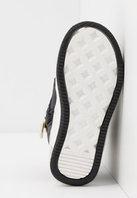 Černé tenisky s texturovanou tkaninou, bílou mezipodešví a gumovou podrážkou. Na boční straně mají zlatý zip a vzorovanou podešev.