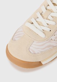 Bottines en suède beige avec un bout, des lacets blancs, une semelle en caoutchouc brun clair et des panneaux en tissu rayé zèbre rose pâle.