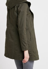 Olivgrön, huppjacka med avslappnad passform, sidoslitsar och långa ärmar. Tillverkad av textil med en mjuk yta.