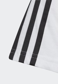 Camiseta deportiva blanca con tres rayas verticales negras en la manga, con un detalle de costura visible a lo largo del dobladillo.