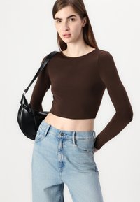 Brun, langermet crop topp kombinert med lyseblå høytlivsbukser og en svart håndveske. Glatt stoff med en tettsittende silhuett.