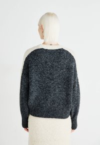 Maglione a maglia grossa con corpo sfumato in nero e grigio e scollatura a coste color crema. Vestibilità rilassata con spalle scese e maniche lunghe.