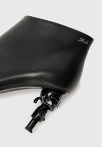 Black leather accessory with a smooth texture, featuring a glossy black hardware attachment and a small silver logo detail.