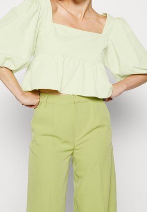 Kvinde iført lys grøn cropped bluse med pufærmer og matchende højtaljede vidde bukser med hænderne på hofterne.