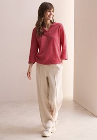 Rot-weiße gestreifte Bluse mit V-Ausschnitt und Dreiviertelärmeln, kombiniert mit cremefarbenen, weit geschnittenen Hosen und weißen Sneakers.