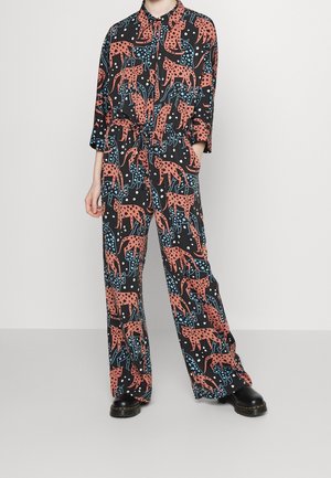 Kombinezon z długim rękawem, z czarną bazą, czerwonymi wzorami w panterkę i niebieskimi akcentami. Ma luźny krój i kołnierzyk zapinany na guziki.