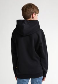 Sweatshirt à capuche noire en tissu doux, avec une grande capuche et des poignets côtelés. Le dos présente un design minimaliste sans graphismes.