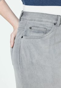 Šedé džíny z denimu s přiléhavým střihem, se zadní kapsou a kovovými detaily. Textura vypadá hladce s jemným vyblednutím.