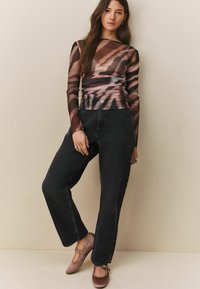 Haut à manches longues en matière transparente, avec un motif tie-dye brun et beige, associé à un jean noir taille haute et des ballerines roses. Détail de tissu texturé visible.