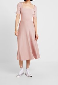 Robe rose clair côtelée avec un décolleté carré et des manches courtes, dotée d'une jupe midi évasée, associée à des baskets montantes blanches.