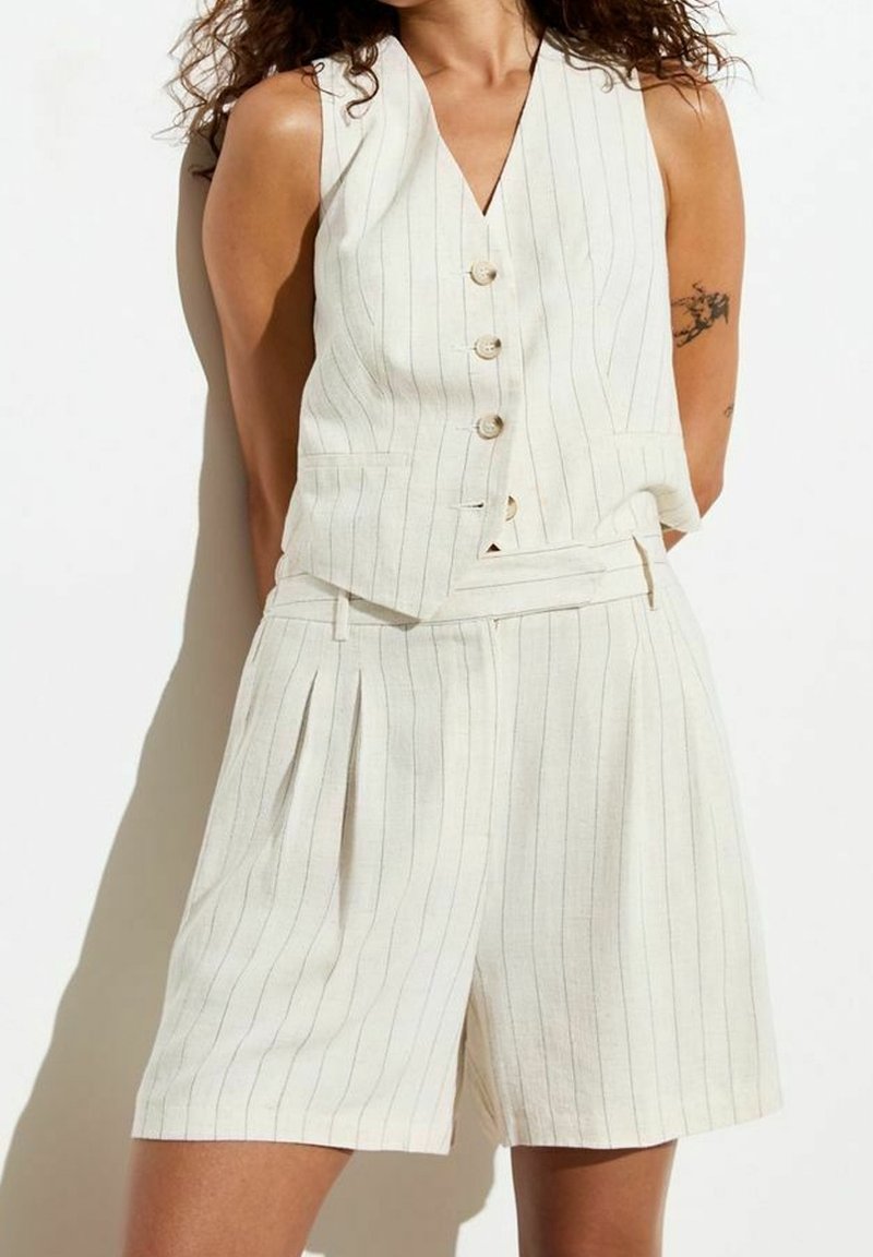 Ljusgräddfärgad, randig tyg, ärmlös väst med fem knappar och matchande shorts med veck, vilket ger en strukturerad, skräddarsydd look.