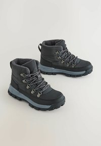 Czarne wodoodporne buty trekkingowe z trwałymi gumowymi podeszwami, szarym sznurowaniem i polarowym wykończeniem. Średni fason dla wsparcia kostki.