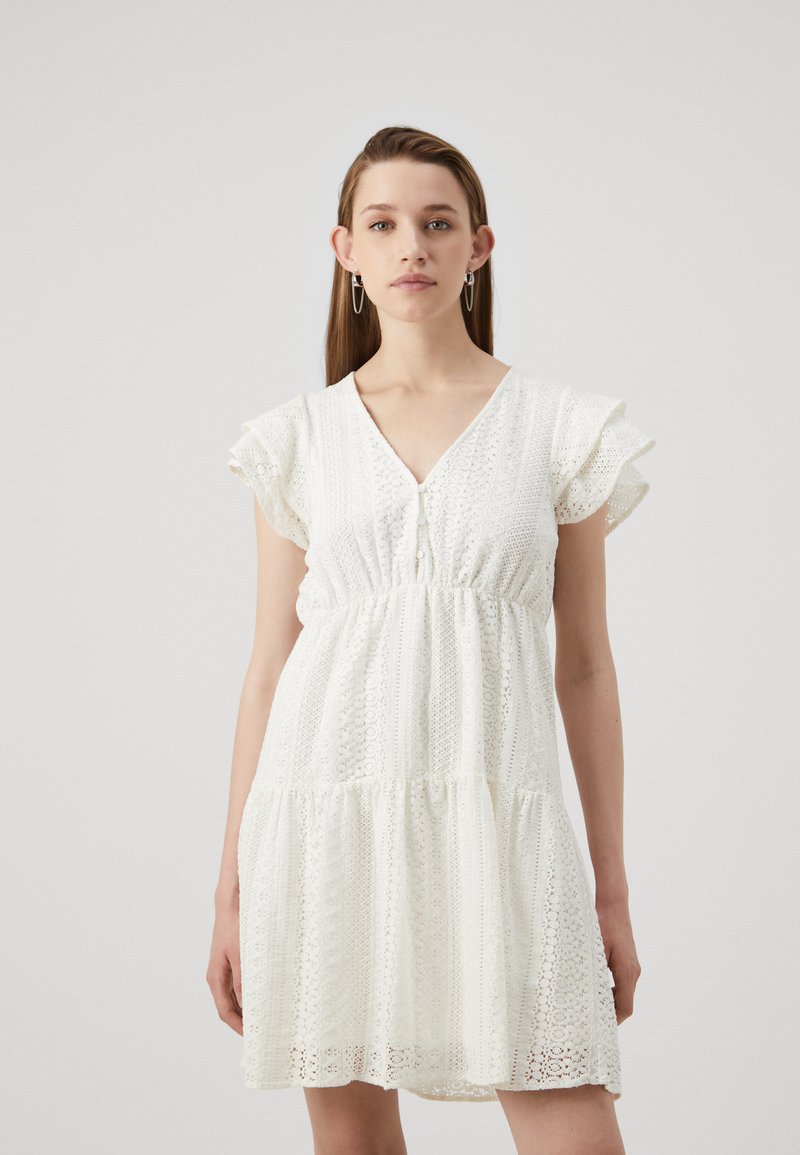 White dress with short, ruffled sleeves, a V-neckline, and a gathered waist. Features intricate lace detailing and a tiered skirt design.