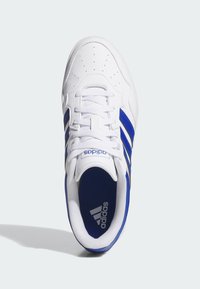 Zapatillas blancas con tres franjas azules. Cuenta con una parte superior perforada, cordones planos y una lengua acolchada. El logo de la marca es visible en el lado.