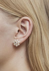 Pendientes en forma de flor con un racimo de perlas blancas y un acento central plateado, enmarcados por un cabello rubio claro.