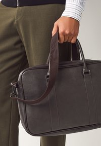 Dunkelbraune Lederhandtasche mit strukturierter Oberfläche, zwei Griffen und verstellbarem Schultergurt, ausgestattet mit dezenten Ziernähten und Metallbeschlägen.