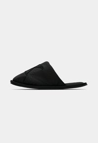 Sandal negru, tip slip-on, cu un upper moale, texturat și o talpă plată. Dispune de un design subtil curbat și accente de cusătură minimaliste.