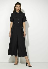 Zwart tweedelig outfit bestaande uit een kortärmelige overhemd met knopen en zakken, en wijde pantalons. Glad fabric met een comfortabele pasvorm.