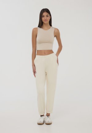 Top corto beige con scollatura rotonda, abbinato a pantaloni jogger color crema chiaro con cintura elasticizzata e polsini.
