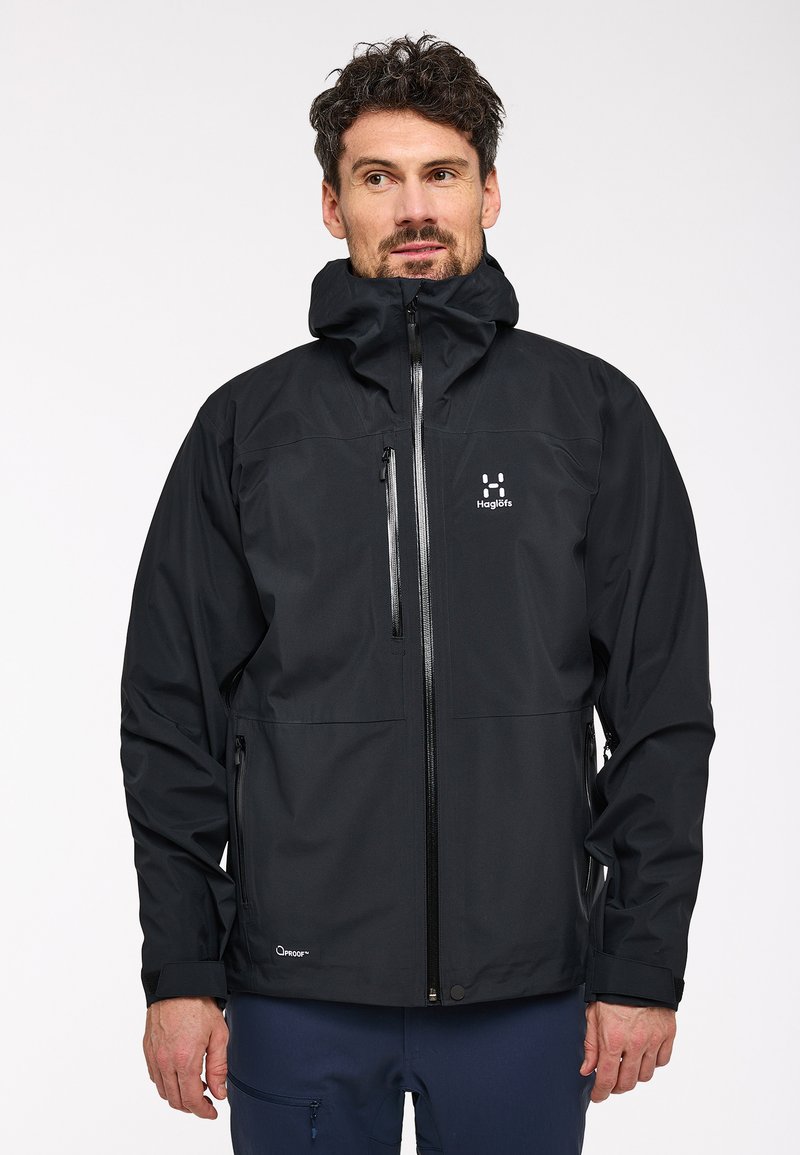 Veste noire imperméable avec fermeture éclair sur le devant, capuche ajustable, deux poches latérales et logo sur la poitrine. Tissu lisse et design ajusté.