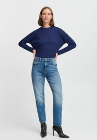Maglione a coste navy con maniche larghe, abbinato a jeans dritti azzurri e stivaletti neri a punta. Design semplice e moderno.