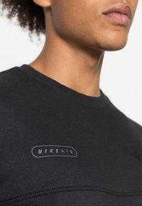 Svart bomullströja med rund halsringning, prydd med en subtil "NIKE AIR"-logotyp i ljusblått tryck på bröstet, mjuk textur och sydda sömmar.