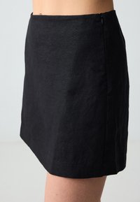 Mini jupe en lin noir au design simple, avec une texture lisse et une fermeture éclair discrète sur le côté.