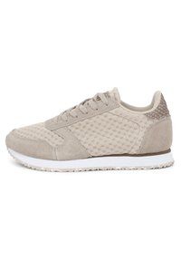 Chaussure de sport beige avec un dessus en daim et en mesh, accent de talon texturé, semelle intermédiaire blanche et semelle extérieure en caoutchouc à motifs.