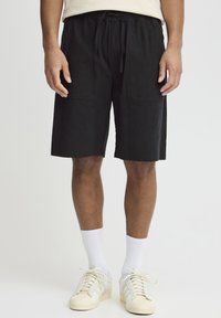 Sorte, knæhøje shorts med en afslappet pasform, der har to frontlommer og en elastisk talje med snøre. Båret med hvide sokker og sneakers.