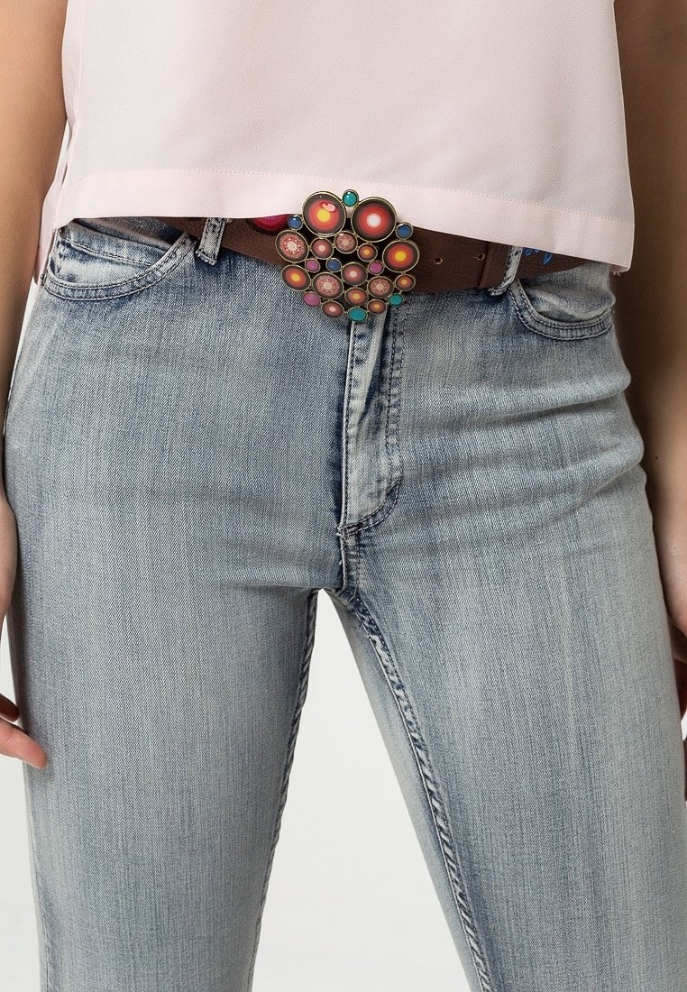Jean bleu clair associé à une ceinture marron avec une grande boucle circulaire colorée et un top court rose pâle.