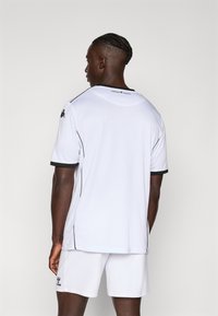 Hvit athletic jersey med svarte aksenter, korte ermer og rund hals. Lett, teksturert stoff, kombinert med matchende shorts.