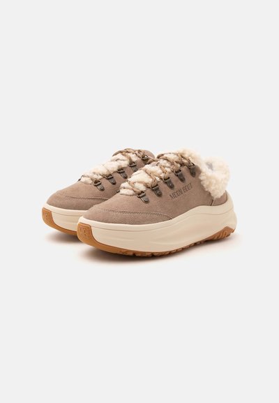 Paire de baskets beige en daim à enfiler avec semelles épaisses blanches, œillets métalliques, laçage à l'avant et doublure blanche et duveteuse autour du col.