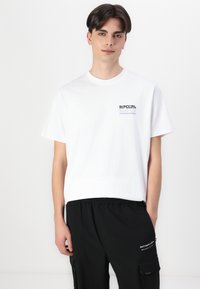 Witte katoenen t-shirt met een klein zwart "RIP CURL" logo op de borst, gecombineerd met zwarte cargobroeken met zijzakken en tekstaccenten.