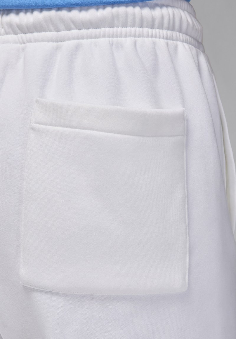 Weiße Sportshorts haben eine weiche, glatte Textur und einen elastischen Taillenbund. Eine rechteckige aufgesetzte Tasche ist auf der Rückseite sichtbar.